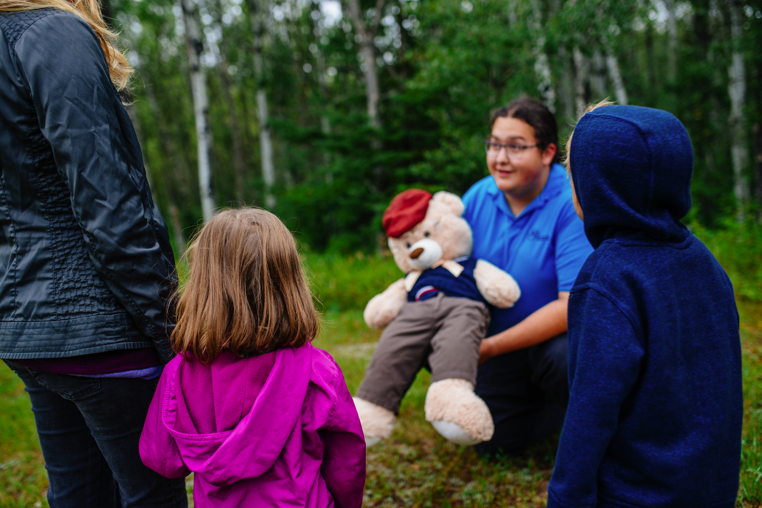 2 children and an adult look on as an interpreter holds a giant stuffed bear.