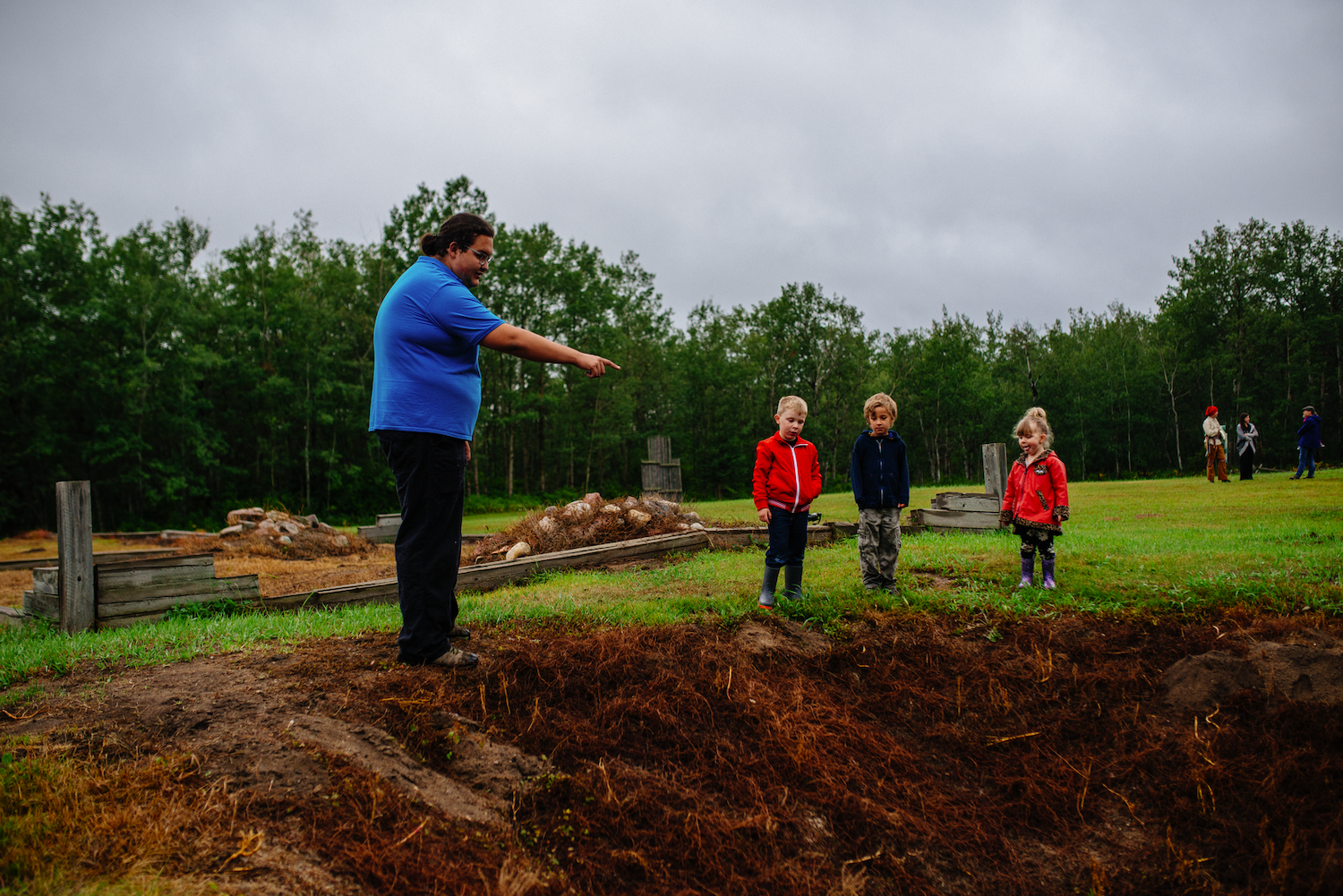 3 small children look into a large hole in the ground as an interpreter standing nearby explains