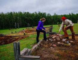 an historical interpreter and a visitor examine mounds of rocks where a building once stood