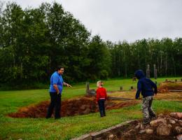 an historical interpreter and two young visitors examine an impression in the ground where a building once stood