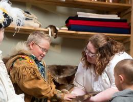 an historical interpreter and three young visitors wearing costumes examine artifacts.